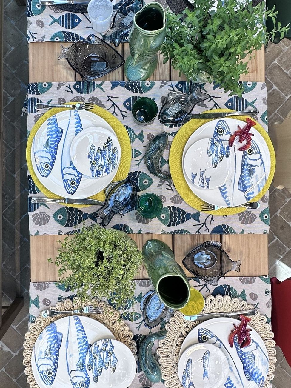 Von oben fotografierter gedeckter Tisch mit handbemalten Fischtellern und Keramikkrügen